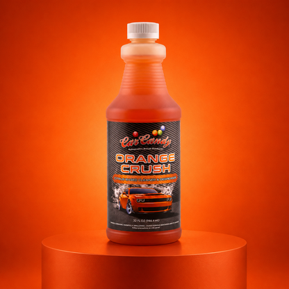 A bottle of Car Candy Orange Crush hand wash cleaner, filled with orange liquid, displayed on a matching orange cylindrical pedestal against a solid orange background.