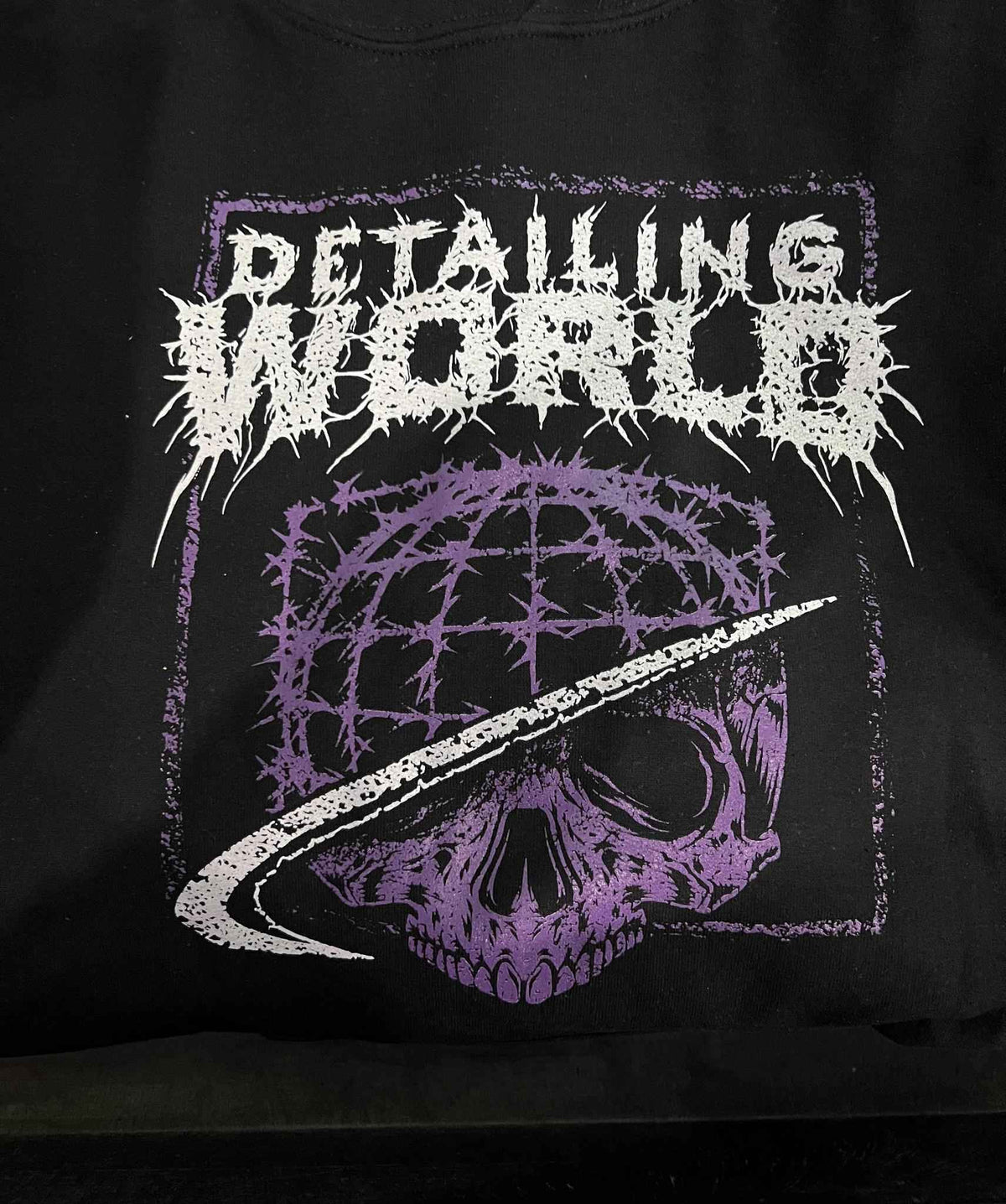 Black t-shirt with white and purple graphic design featuring a skull and text on a black background.